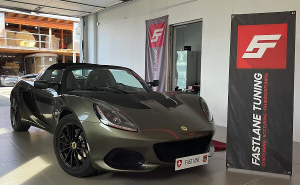 Ein olivgrün/grauer Lotus Elise 3 Sport 220 steht neben dem Banner der Fastlane Tuning Schweiz GmbH