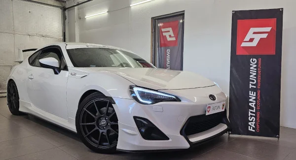 Ein weißer Toyota GT86 steht neben dem Banner der Fastlane Tuning Schweiz GmbH