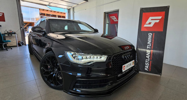 Neben dem Banner der Fastlane Tuning Schweiz GmbH steht ein schwarzer Audi S6 Kombi