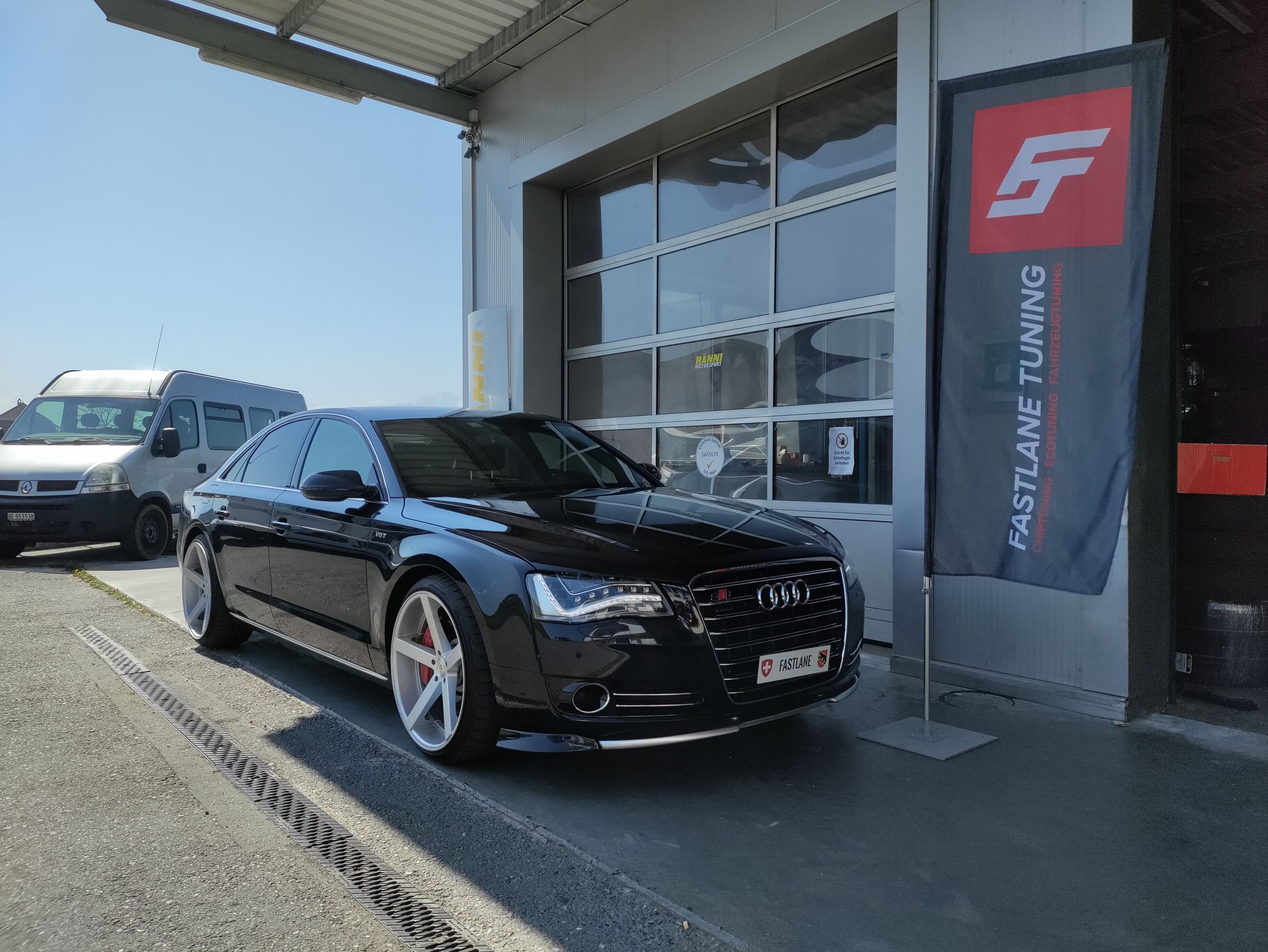 Ein schwarzer Audi A8 4.2 Liter V8 TDI steht vor der Garage neben der Fastlane Tuning Schweiz Flagge