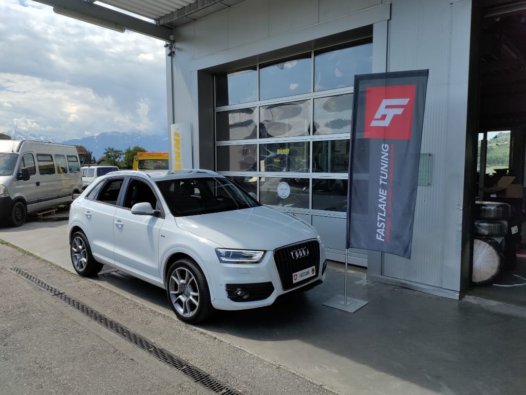 Ein weisser Audi Q3 2.0 TDI parkiert vor der Garage neben der Fastlane Tuning Schweiz Flagge