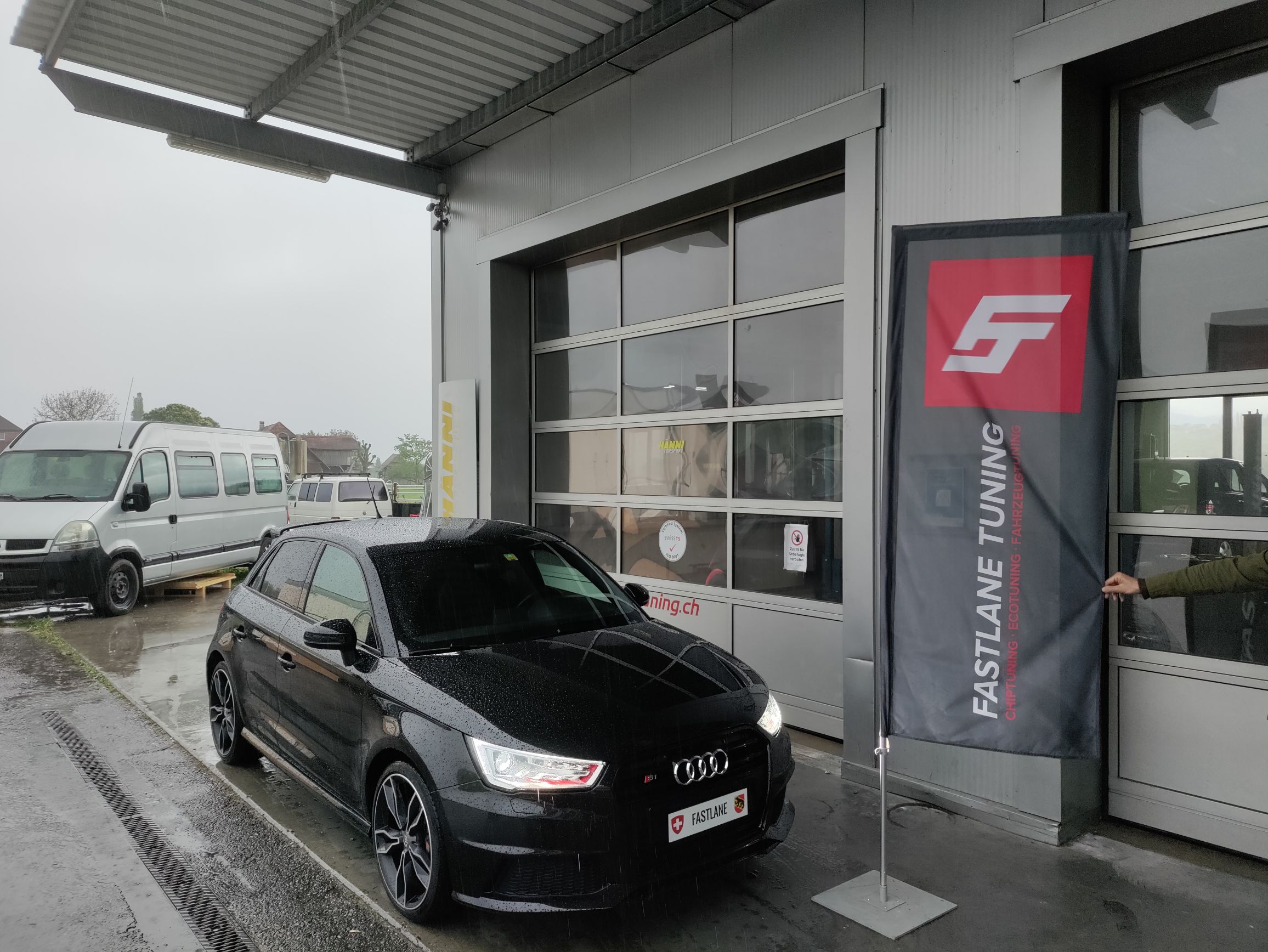 Ein schwarzer Audi S1 parkt vor der Garage neben der Fastlane Tuning Schweiz-Fahne