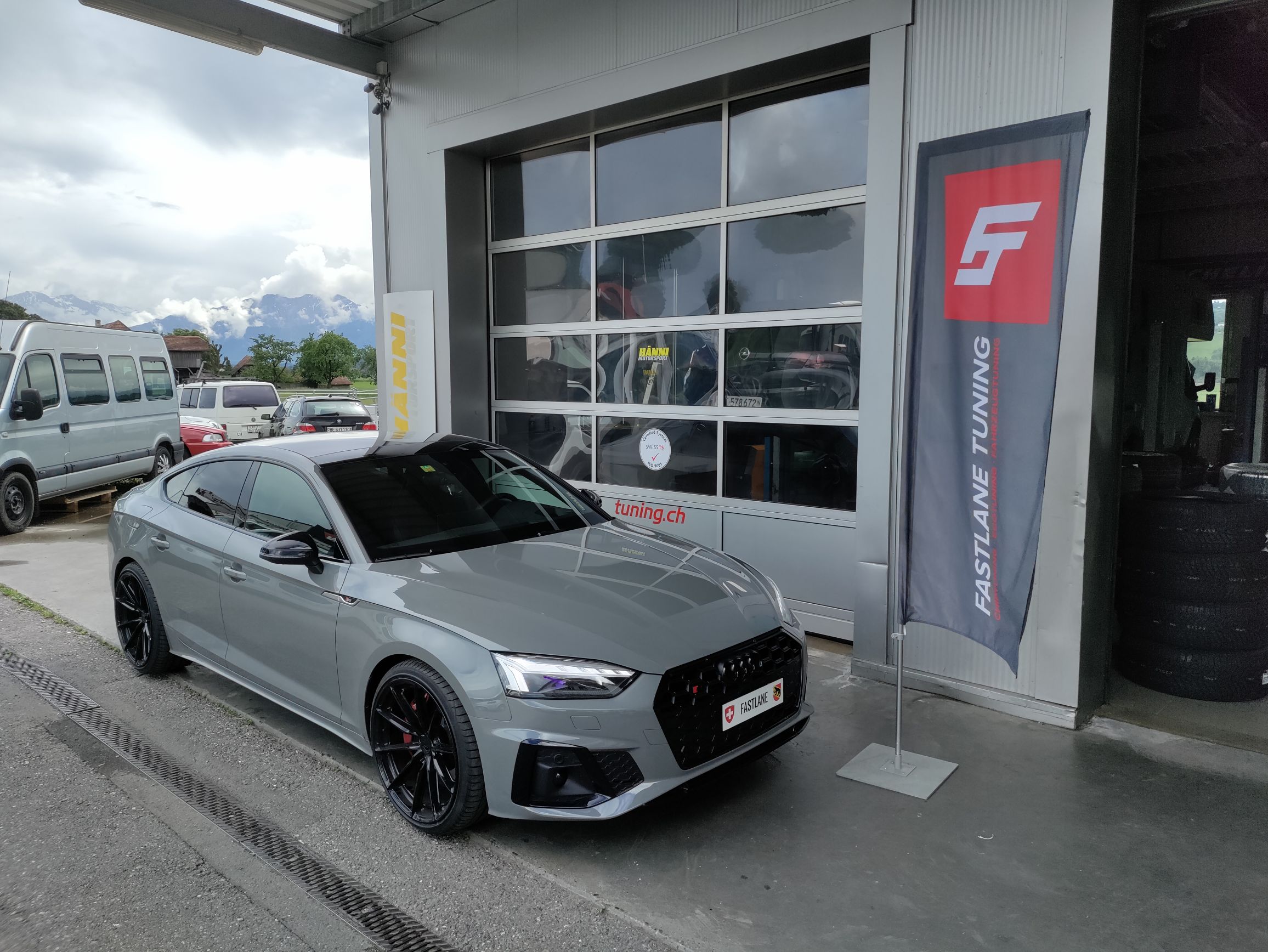 Ein mattgrauer Audi S5 TDI Sportback steht vor der Garage neben der Fastlane Tuning Schweiz Flagge
