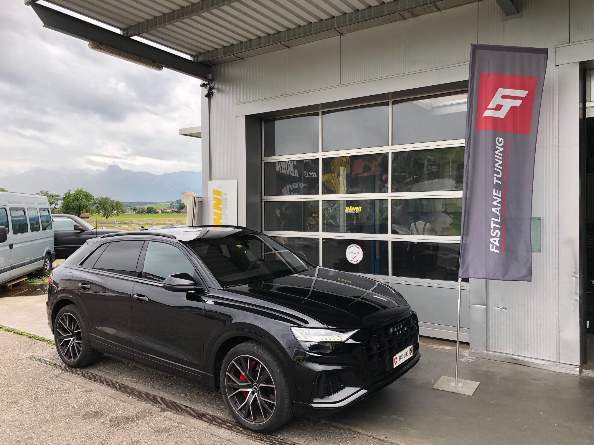 Ein schwarzer Audi SQ8 V8 4.0 Liter mit Doppelturboaufladung steht vor der Garage neben der Fastlane Tuning Schweiz Flagge