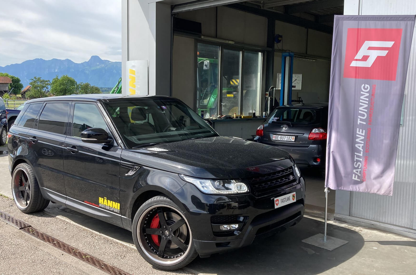 Ein schwarzer Range Rover Sport SDV6 steht neben der Fastlane Tuning Schweiz Flagge.