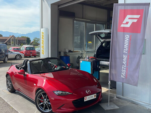 Ein roter Mazda MX-5 steht neben der Fastlane Tuning Schweiz Flagge.