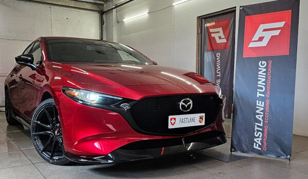 Ein verbrannter roter Mazda 3 2.5 turbo skyactive G steht neben dem Banner der Fastlane Tuning Schweiz GmbH.