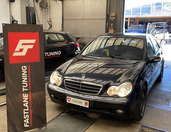 Ein schwarzer Mercedes C200 Kompressor steht neben dem Banner der Fastlane Tuning Schweiz GmbH
