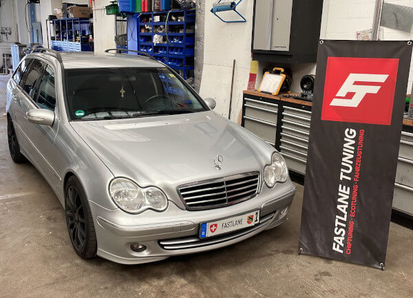 Ein silberner Mercedes Benz C200 Kombi steht neben dem Banner der Fastlane Tuning Schweiz GmbH