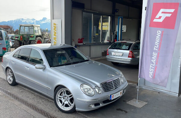 Ein silberner Mercedes Benz E240 steht neben der Fastlane Tuning Schweiz Flagge