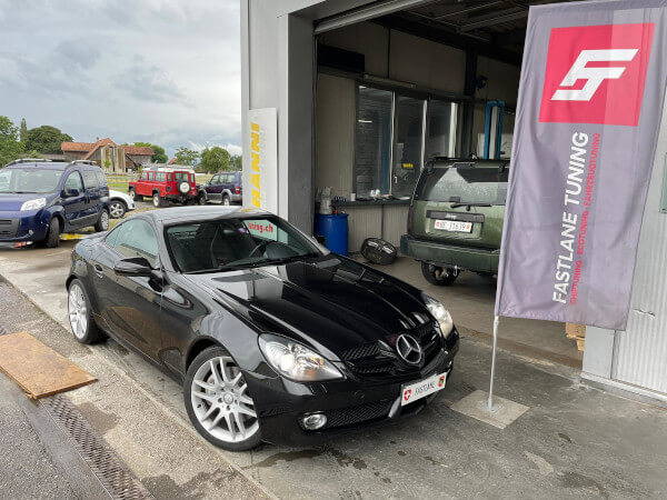 Ein schwarzes Mercedes SLK 280 V6 2-Türer Cabrio steht neben der Fastlane Tuning Schweiz Flagge.