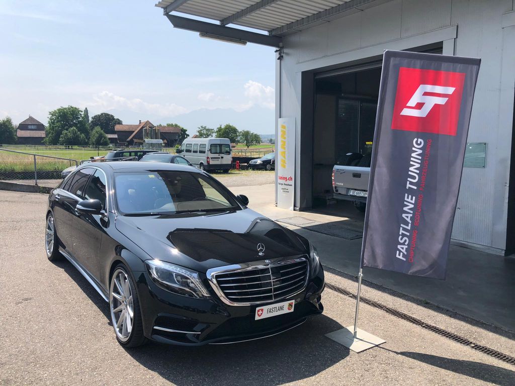 Ein schwarzer Mercedes Benz S500 4.7 Liter V8 steht vor der Garage neben der Fastlane Tuning Schweiz Flagge