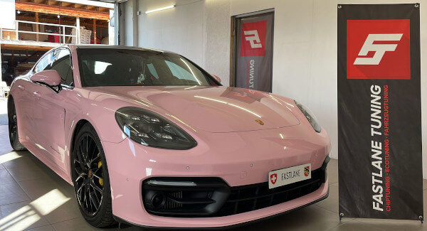 Ein rosa Porsche Panamera 4 steht neben dem Banner der Fastlane Tuning Schweiz GmbH