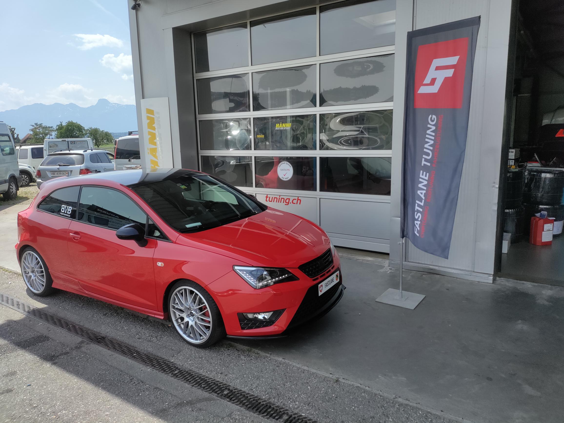 Ein roter SEAT Ibiza 1.4 Liter steht vor der Garage neben der Fastlane Tuning Schweiz Flagge