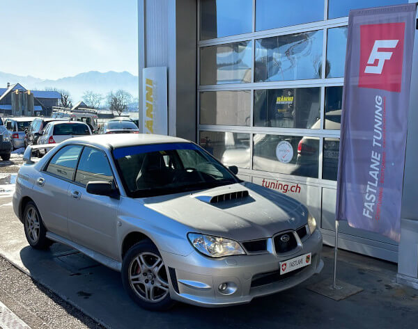 Ein silbernes Subaru Impreza WRX 2006 Modell steht neben der Fastlane Tuning Schweiz Flagge