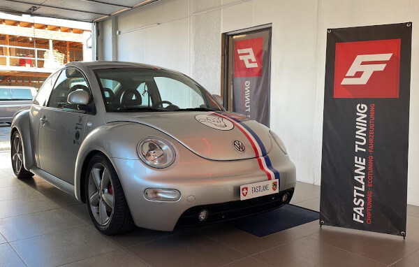 Ein silberner VW-Käfer mit Herbie-Rennstreifen und Hang-Loose-Logo steht neben der Fastlane Tuning Schweiz GmbH-Fahne. Jetzt fährt er wirklich wie Herbie.