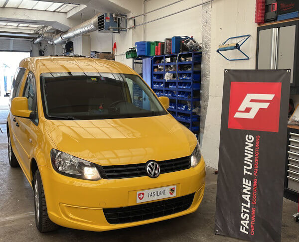 Ein gelber ehemaliger Post Auto VW Caddy steht neben dem Banner der Fastlane Tuning Schweiz GmbH