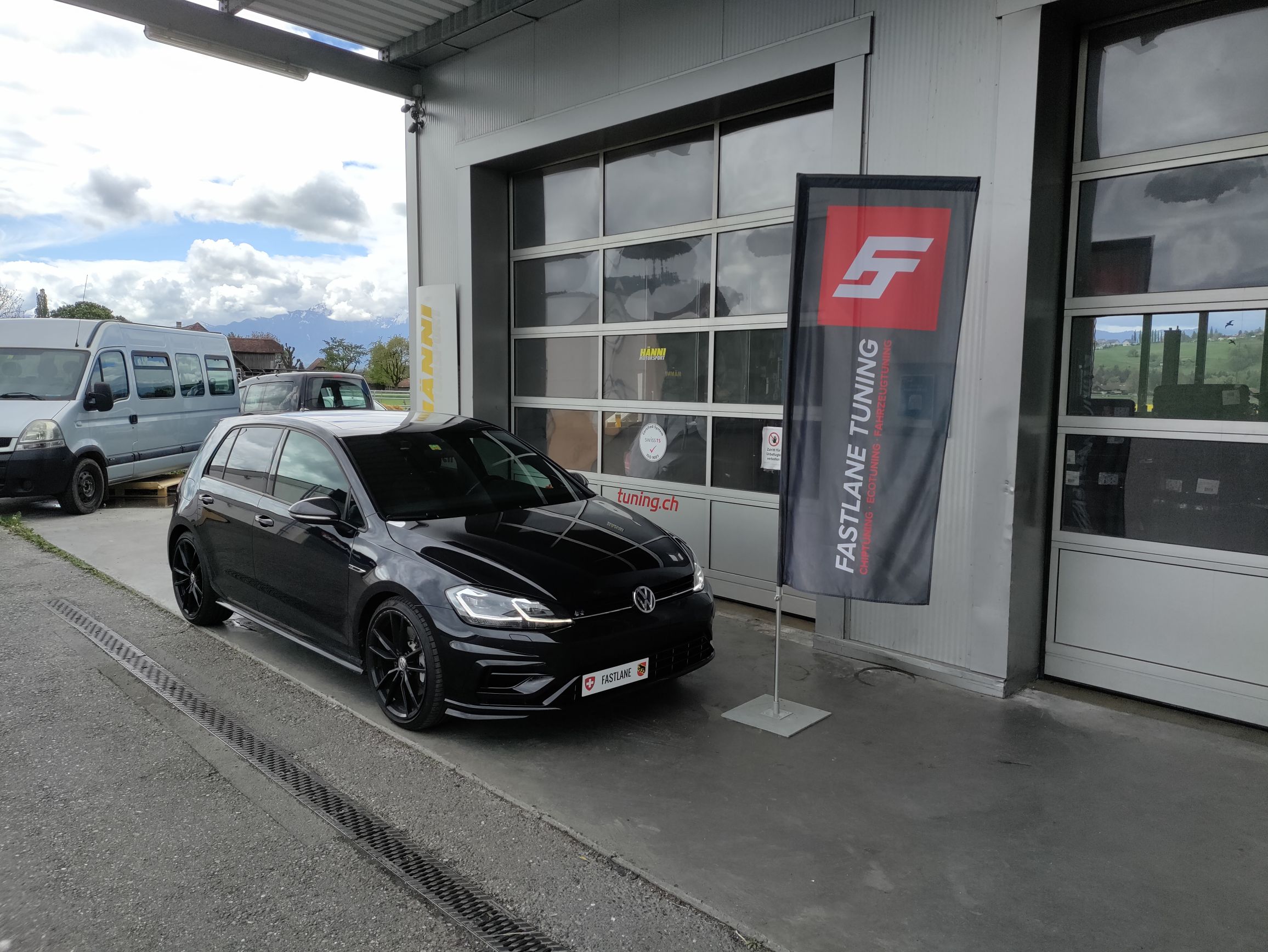 Ein schwarzer Volkswagen Golf 7 R steht vor der Garage neben der Fastlane Tuning Schweiz Flagge