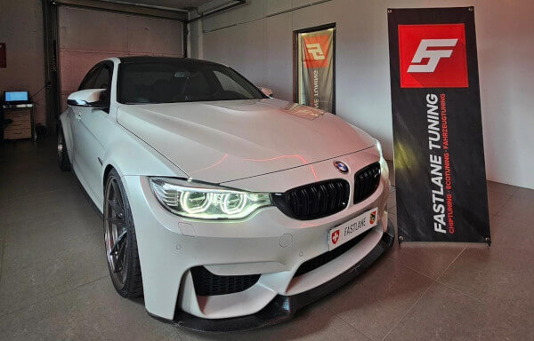 Neben dem Banner der Fastlane Tuning Schweiz GmbH steht ein weißer BMW M3