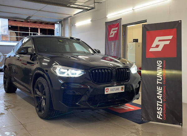 Ein schwarzer BMW X4M Competition steht neben dem Banner der Fastlane Tuning Schweiz GmbH