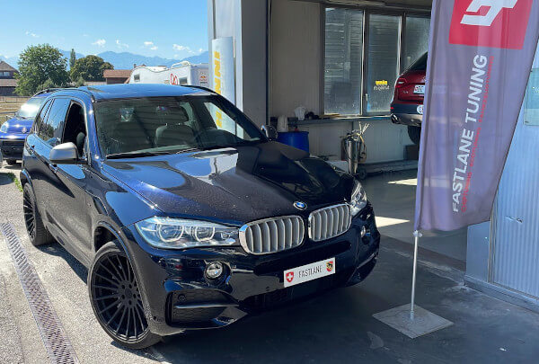 Ein schwarze BMW X5 M50d steht neben das Fastlane Tuning Schweiz flagge