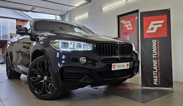 Ein schwarzer BMW X6 50i 4.4 V8 Biturbo steht neben dem Banner der Fastlane Tuning Schweiz GmbH