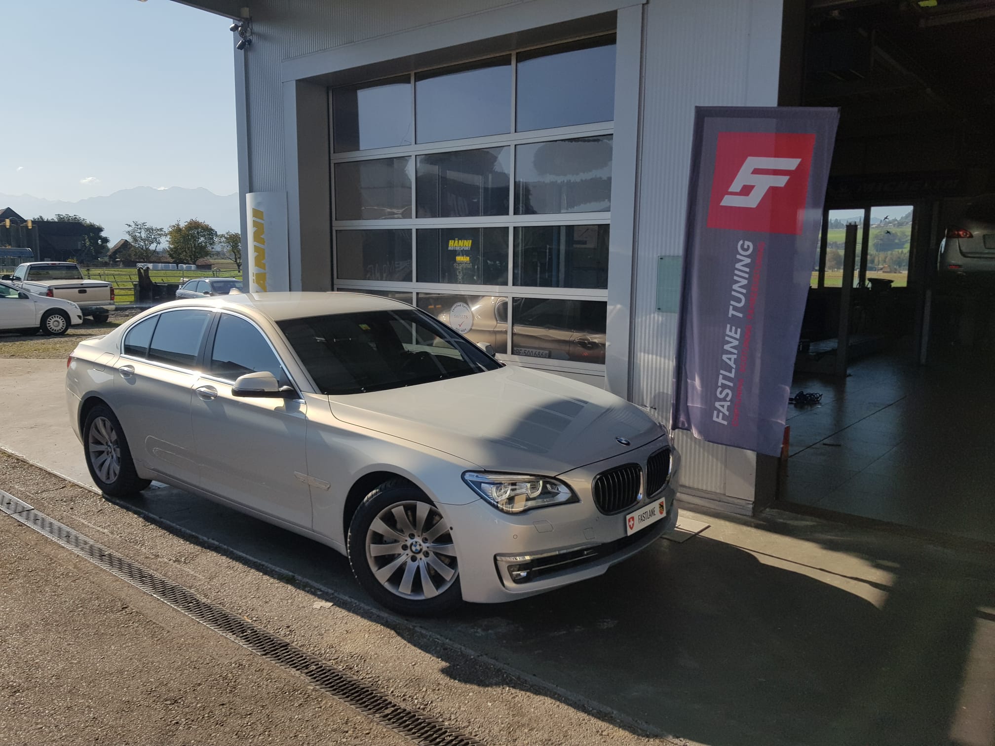 A silver grey BMW 740d xDrive stands next to the fastlane tuning schweiz flag