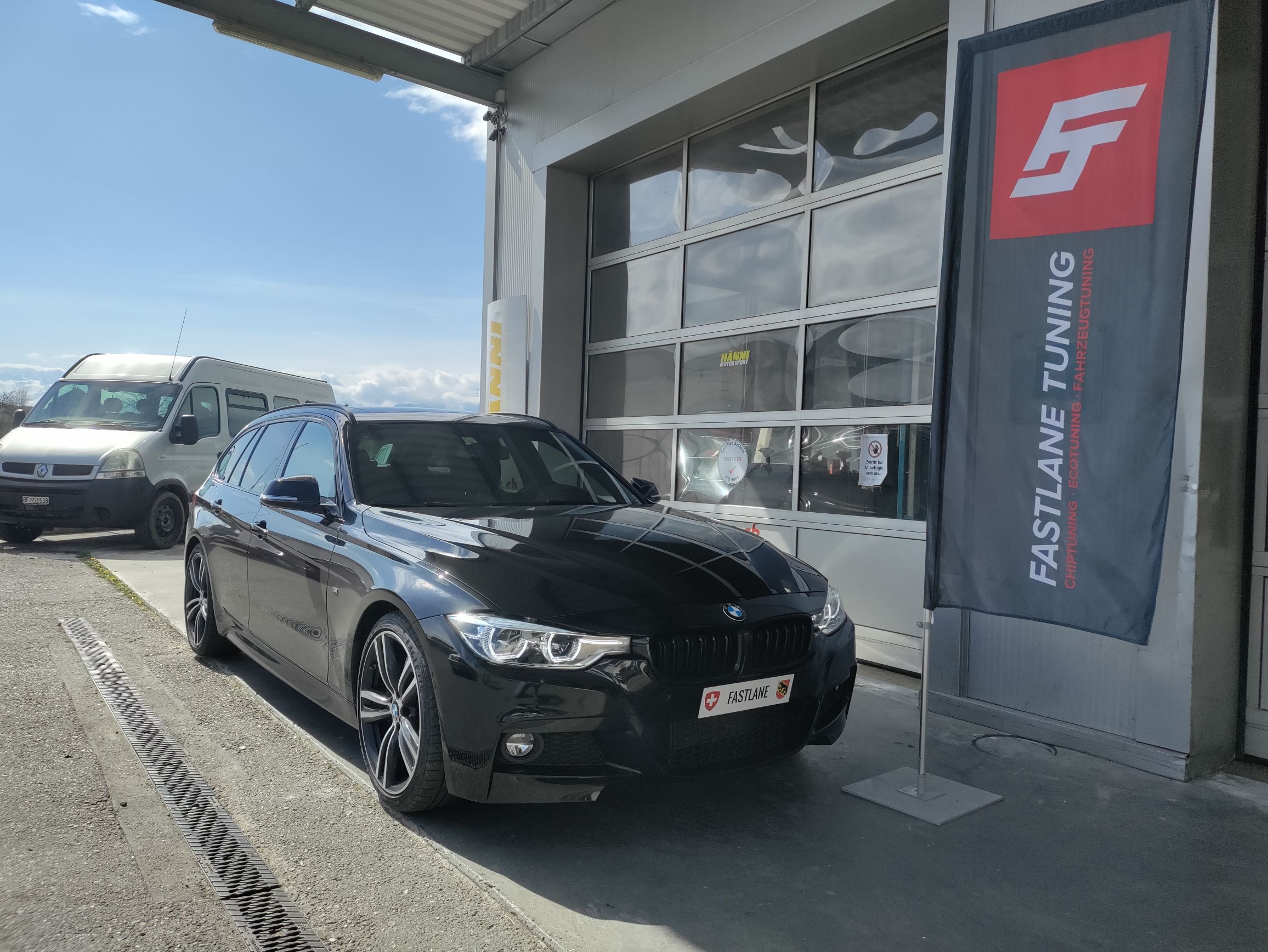 Ein schwarzer BMW F Series 340i Kombi mit B58 Motor steht vor der Garage neben der Fastlane Tuning Schweiz Flagge.