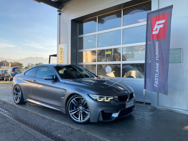 Ein graues BMW M4 Coupe steht vor der Garage von Fastlane Tuning Schweiz.