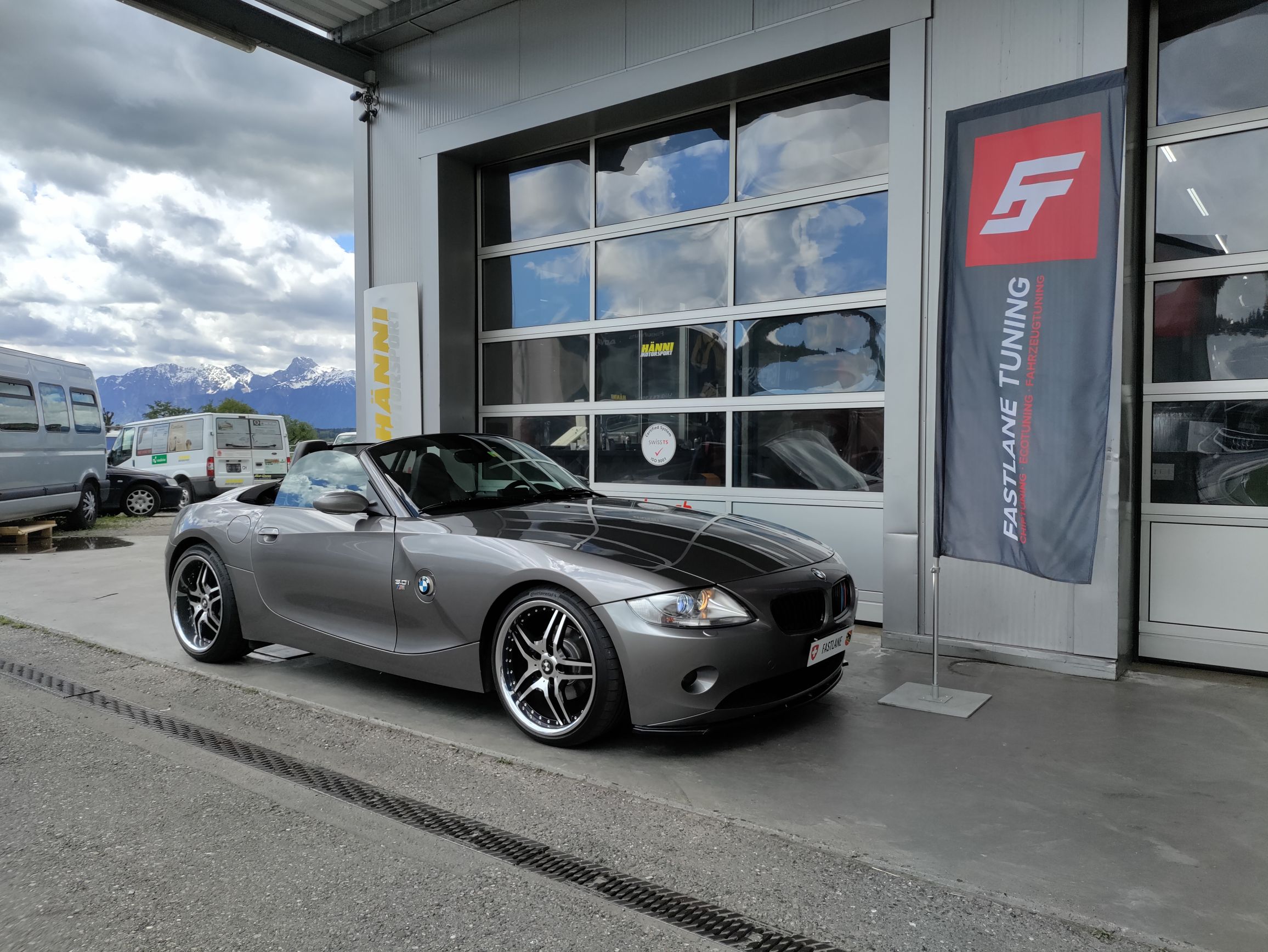 Ein silbergrauer BMW Z4 E Series parkt vor der Garage neben der Fastlane Tuning Schweiz Flagge
